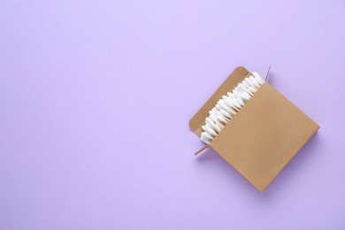 Box with wooden cotton buds on violet background, top view. Space for text