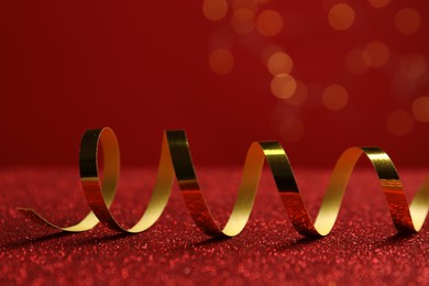 Shiny golden serpentine streamer on red table against blurred lights, closeup