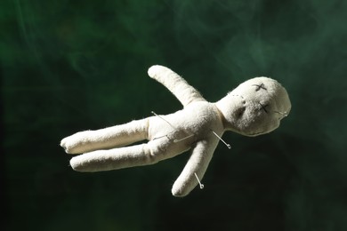 Photo of Voodoo doll with pins and smoke on dark green background