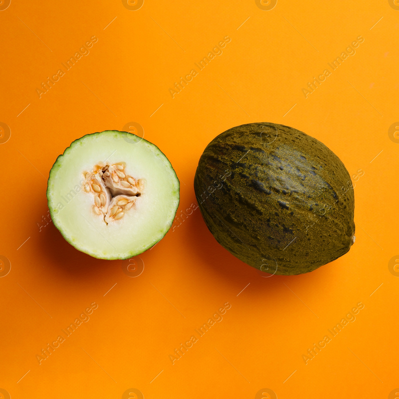 Photo of Ripe tasty melons on orange background, flat lay