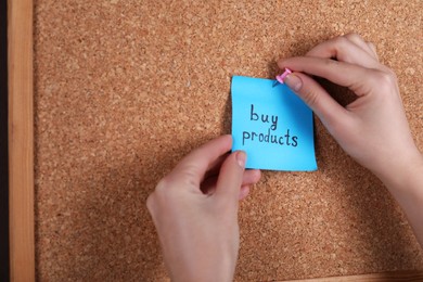 Photo of Woman pinning paper note with phrase Buy Products to cork board, closeup