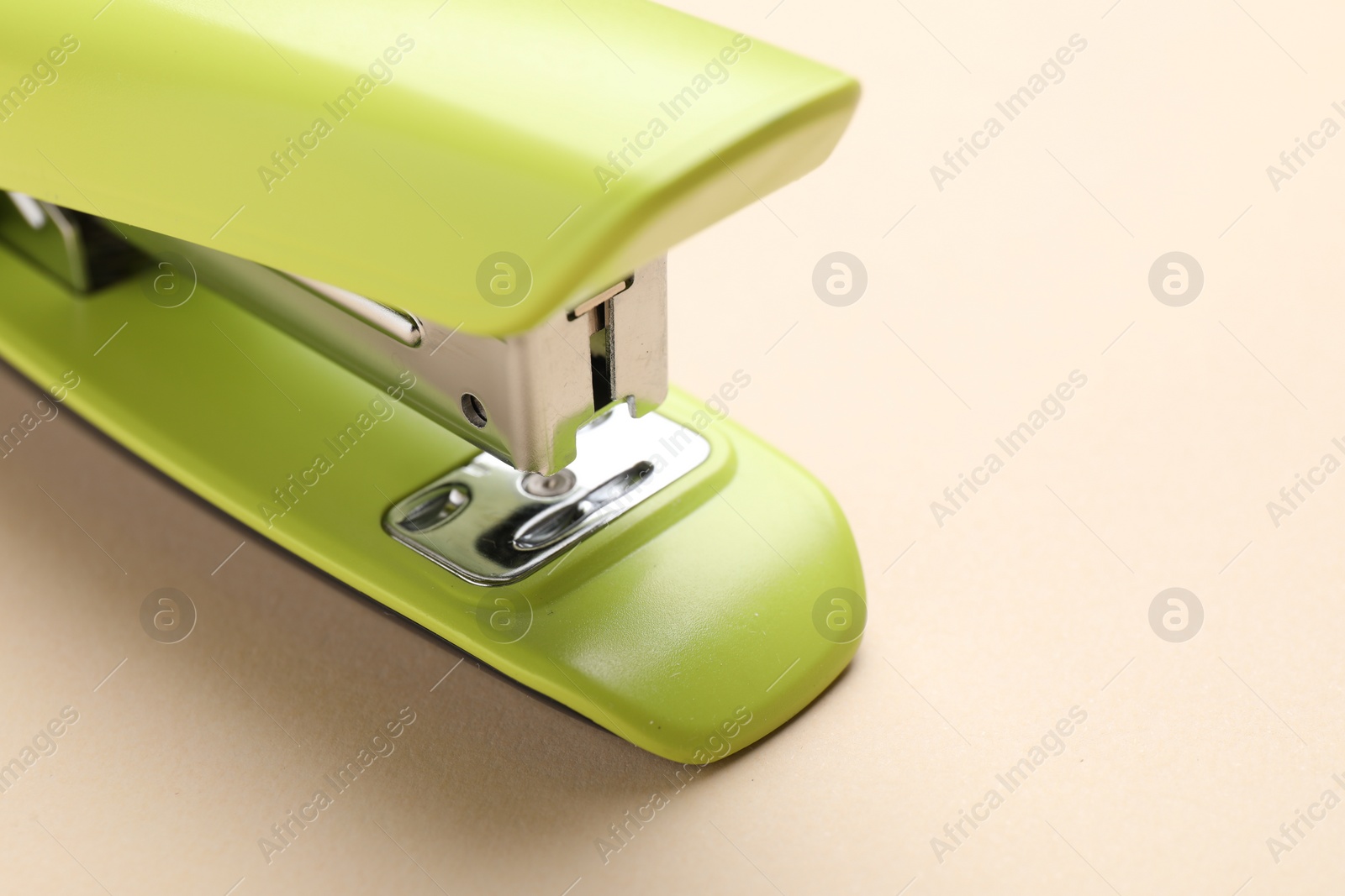 Photo of One bright stapler on beige background, closeup. Space for text