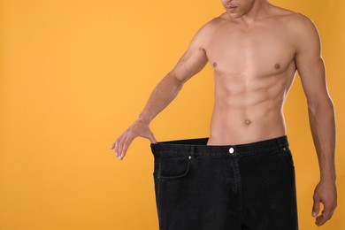 Photo of Shirtless man with slim body wearing big jeans on yellow background, closeup. Space for text