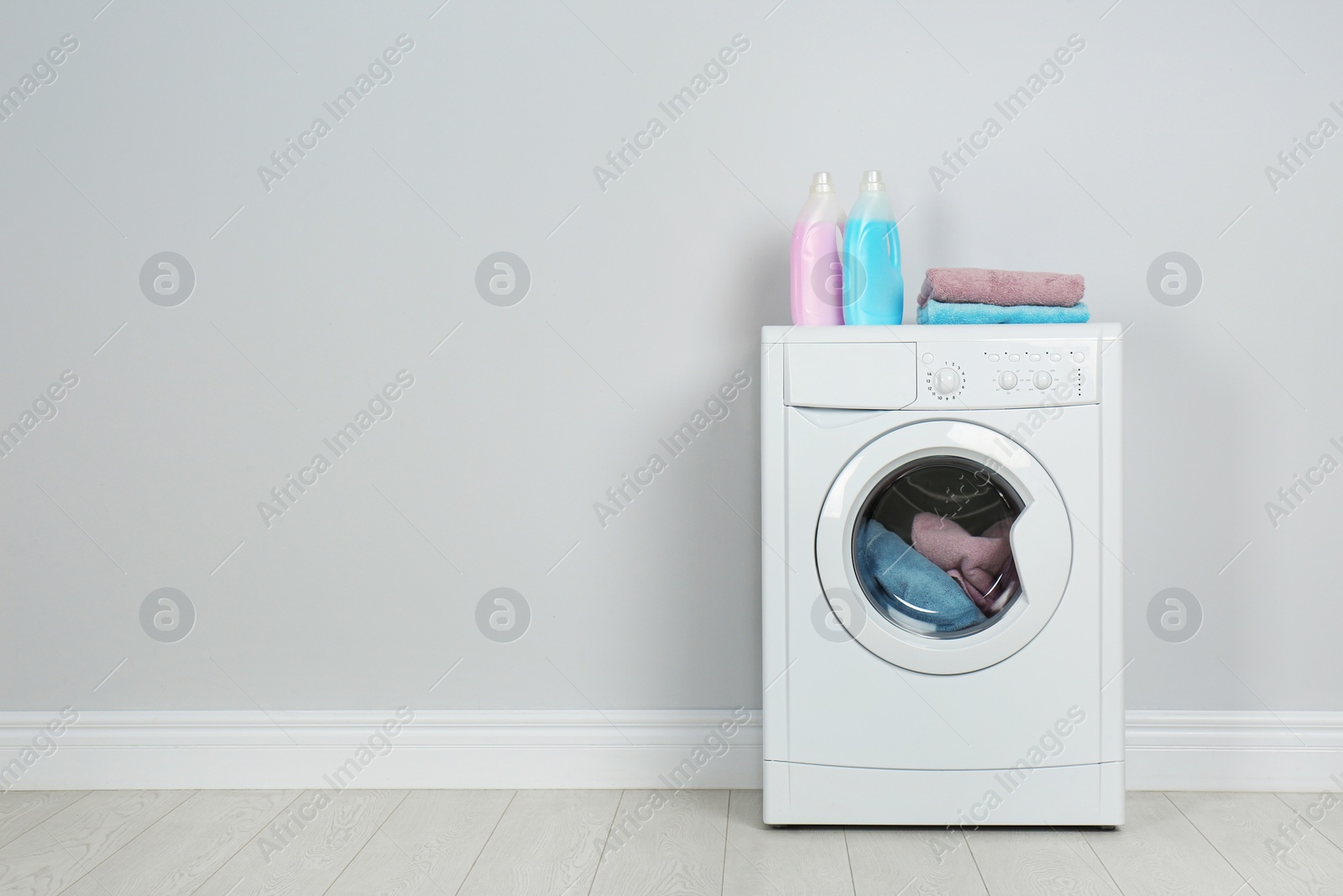 Photo of Modern washing machine with stack of towels and detergents near white wall, space for text. Laundry day