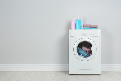 Modern washing machine with stack of towels and detergents near white wall, space for text. Laundry day