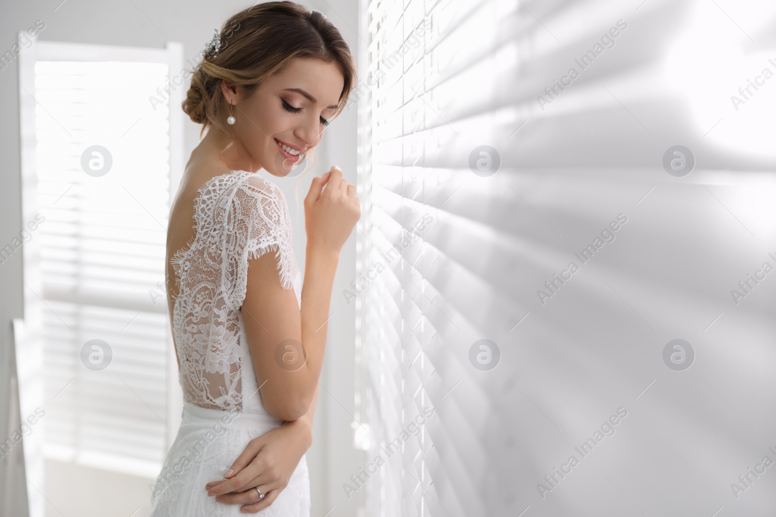 Photo of Young bride with elegant wedding hairstyle near window indoors