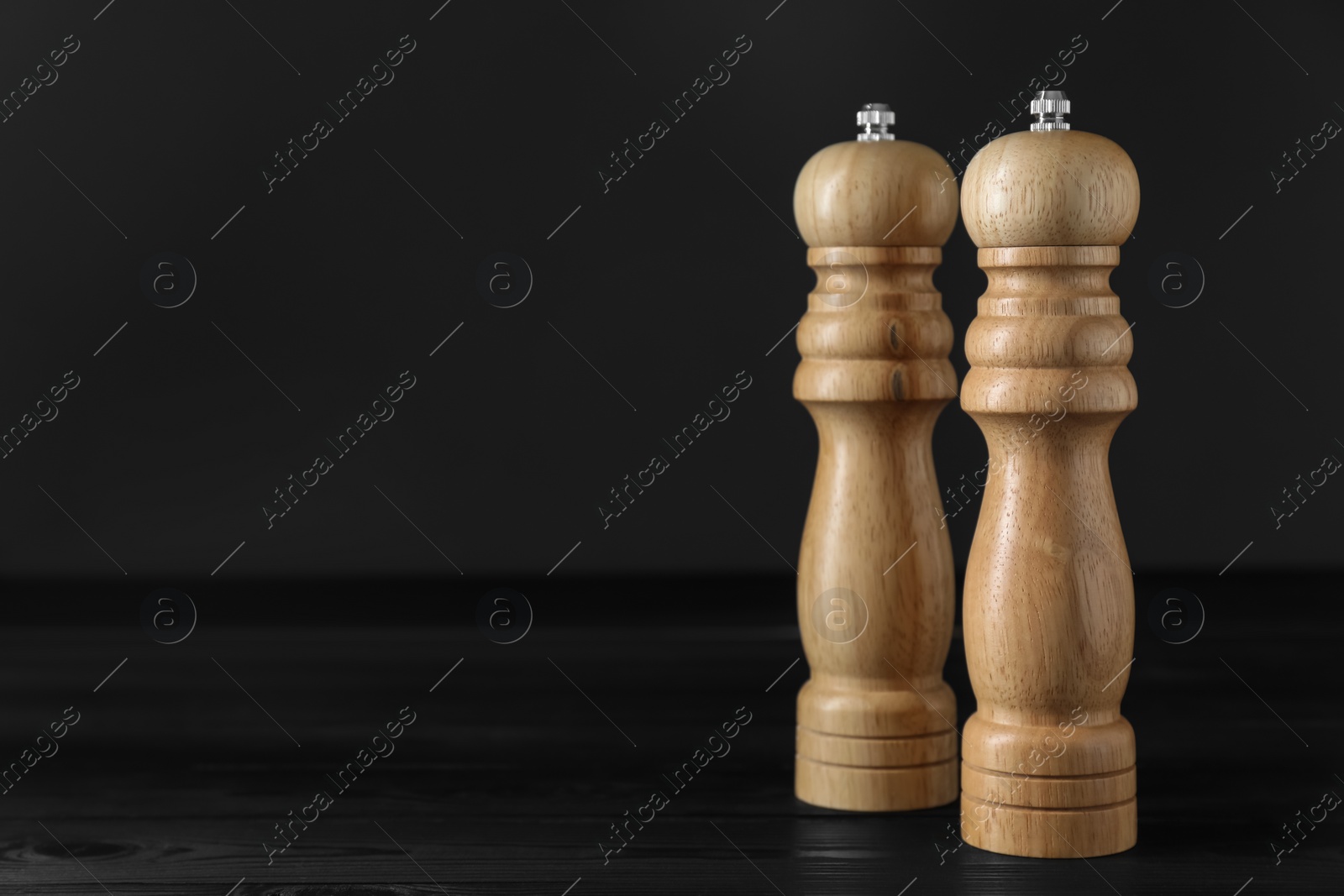 Photo of Salt and pepper shakers on black wooden table, closeup. Space for text