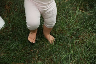 Little child walking on green grass outdoors, closeup. Space for text