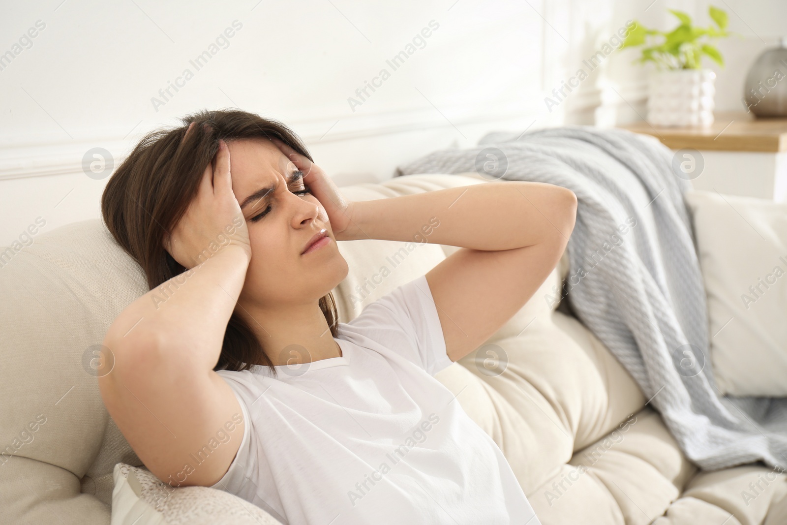 Photo of Young woman suffering from migraine on sofa at home