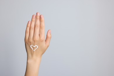 Photo of Heart painted with cream on hand against light grey background, closeup. Space for text