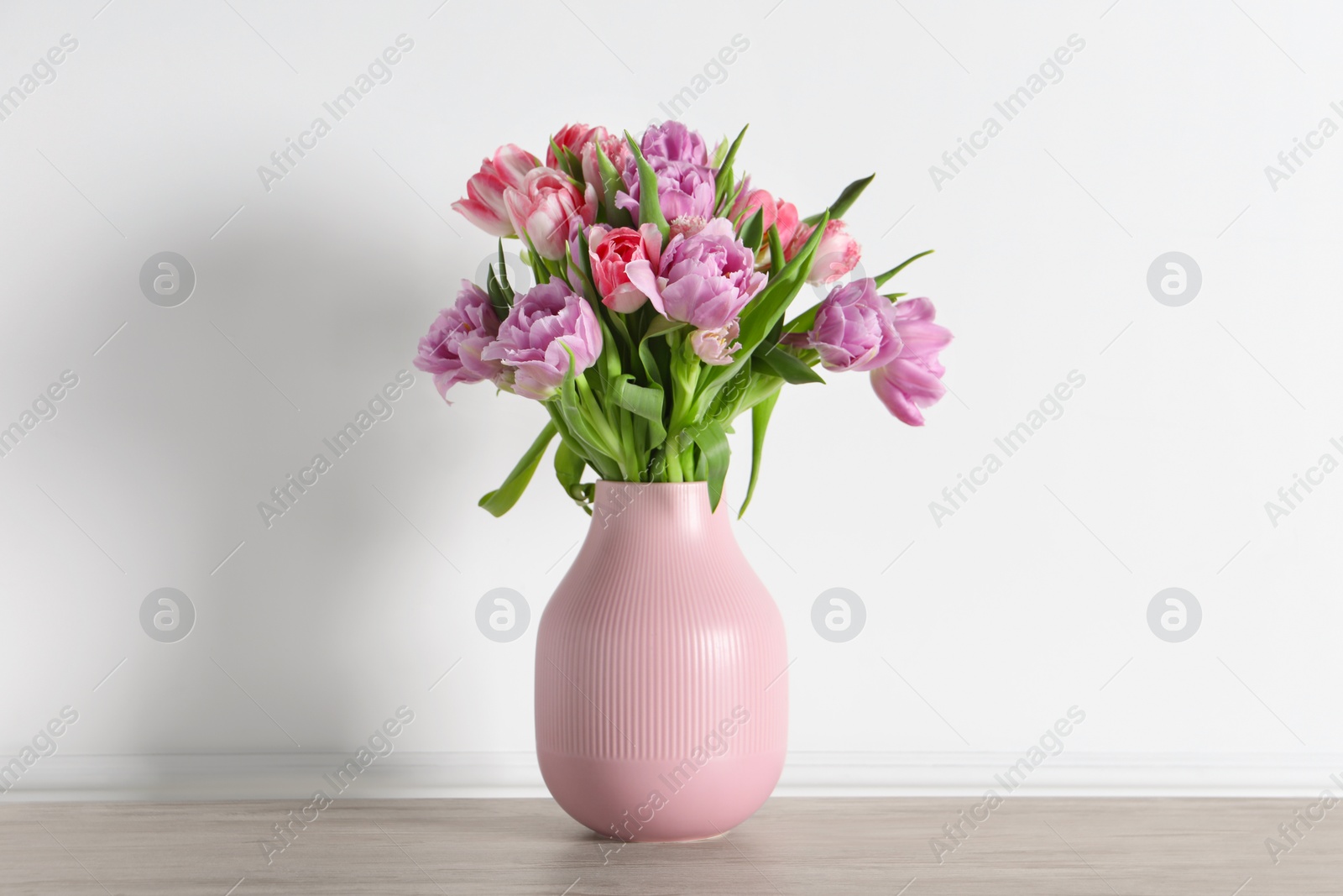 Photo of Beautiful bouquet of colorful tulip flowers on floor near white wall