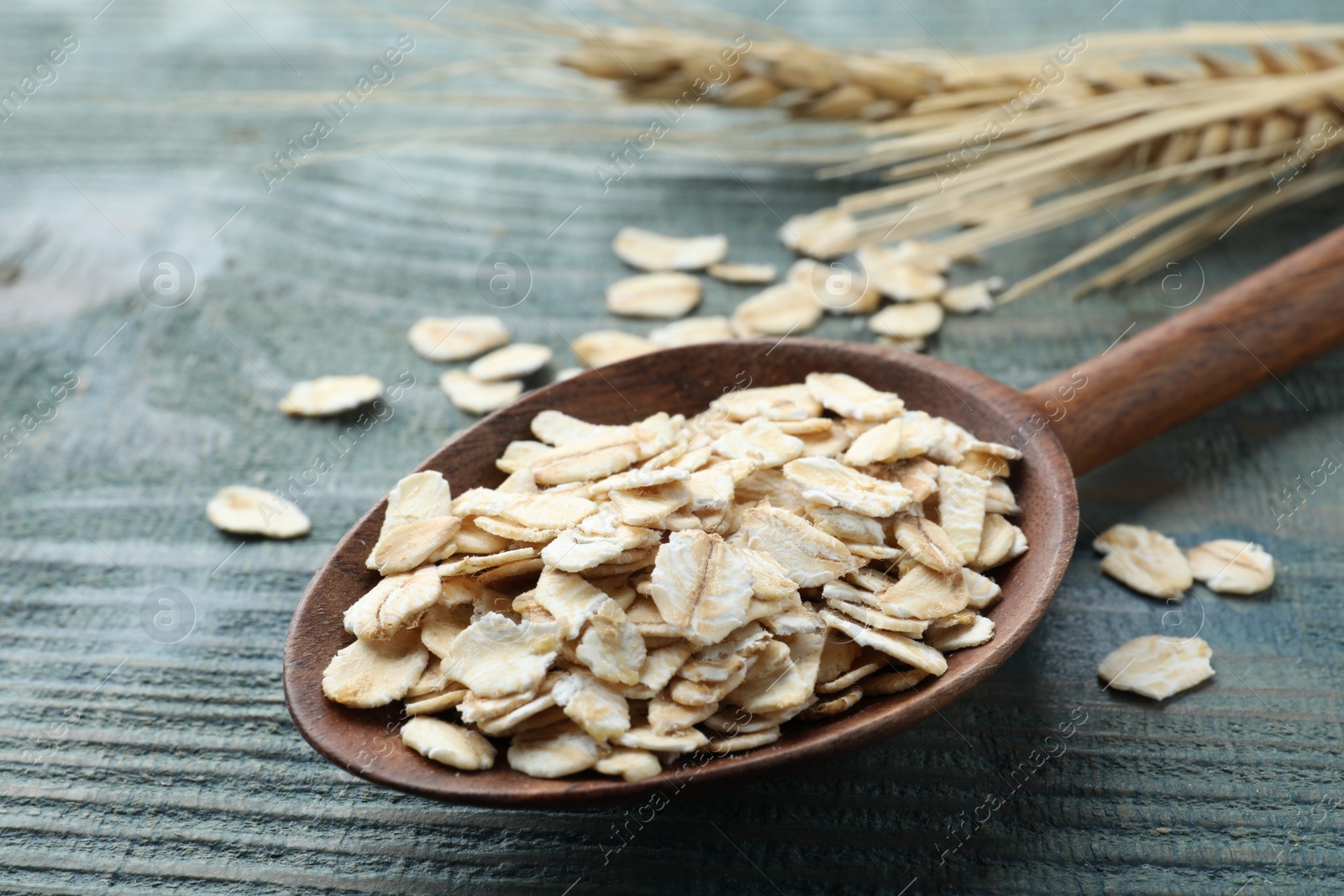 Photo of Spoon with oatmeal on light blue wooden table, closeup