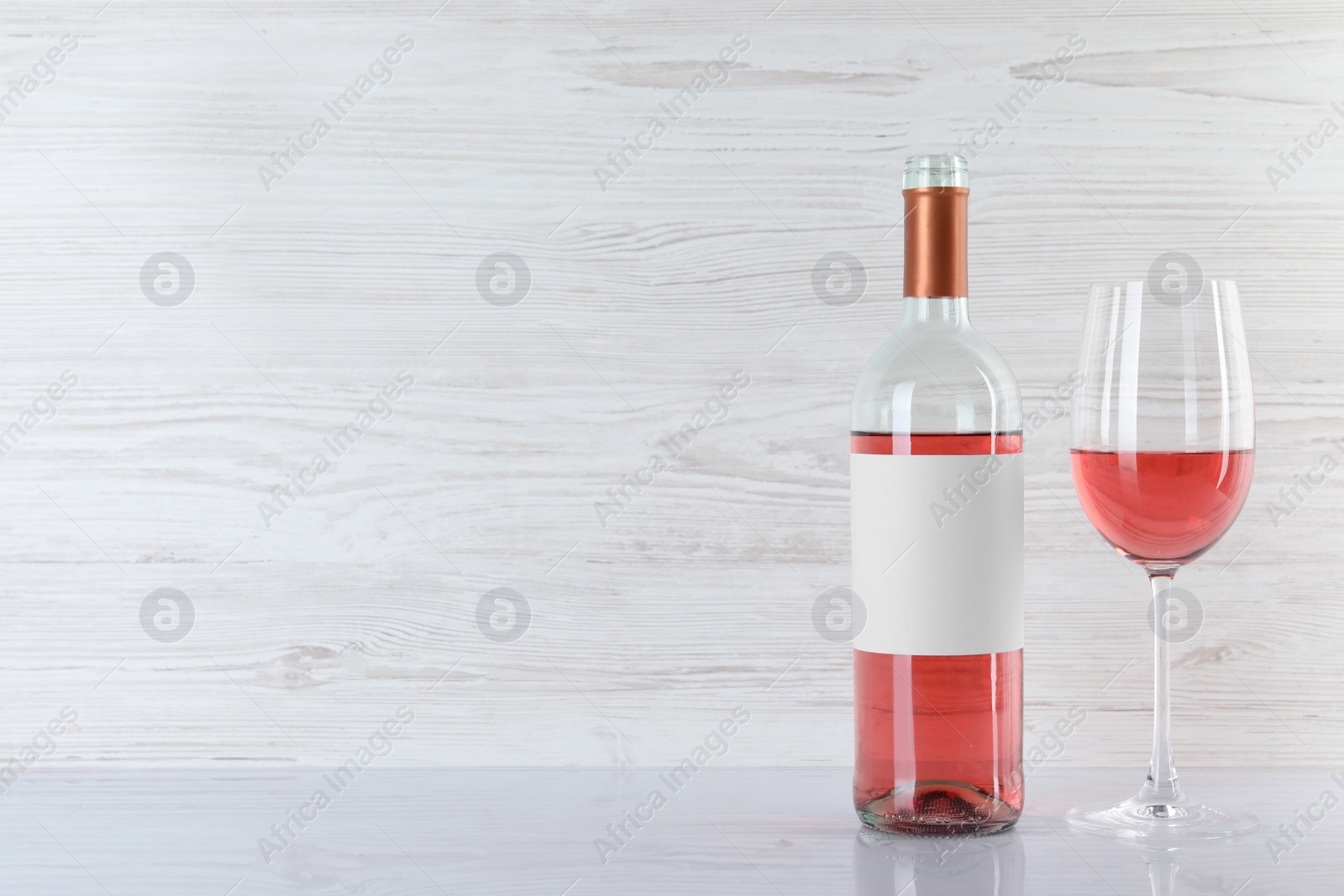 Photo of Bottle and glass of delicious rose wine on table against white wooden background. Space for text