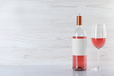 Bottle and glass of delicious rose wine on table against white wooden background. Space for text
