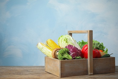 Photo of Different fresh vegetables in crate on wooden table