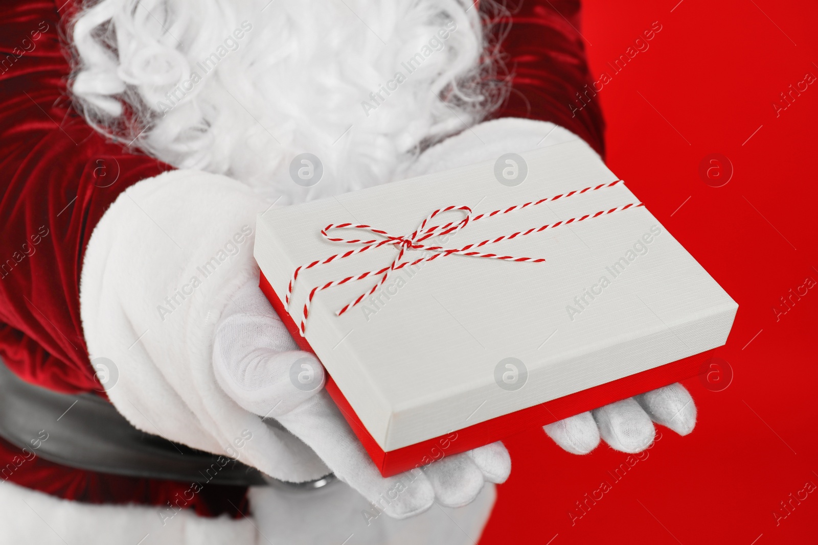 Photo of Santa Claus holding Christmas gift on red background, closeup
