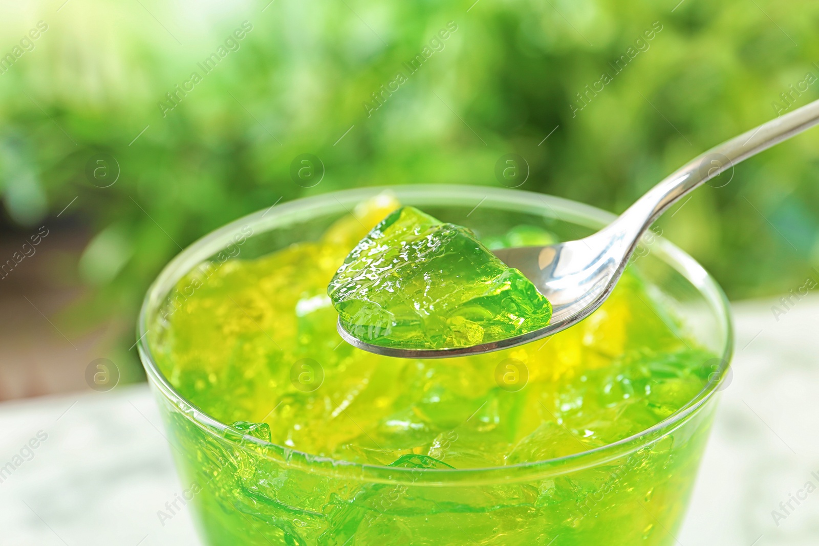 Photo of Spoon with fruit jelly over glass on blurred background, closeup