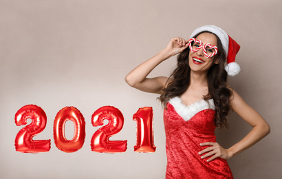 Image of Beautiful woman in Christmas costume and foil 2021 balloons on beige background