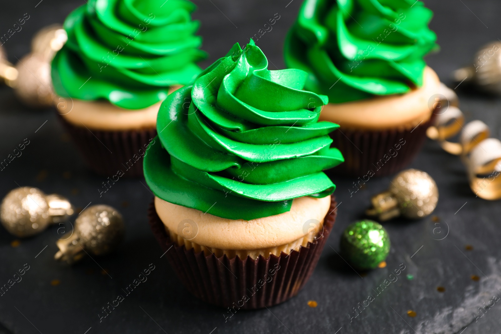 Photo of Delicious cupcakes with green cream and Christmas decor on black table, closeup