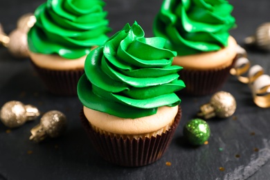 Delicious cupcakes with green cream and Christmas decor on black table, closeup