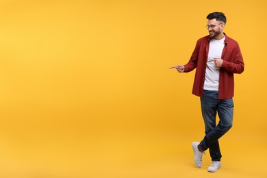 Happy young man pointing at something on yellow background, space for text