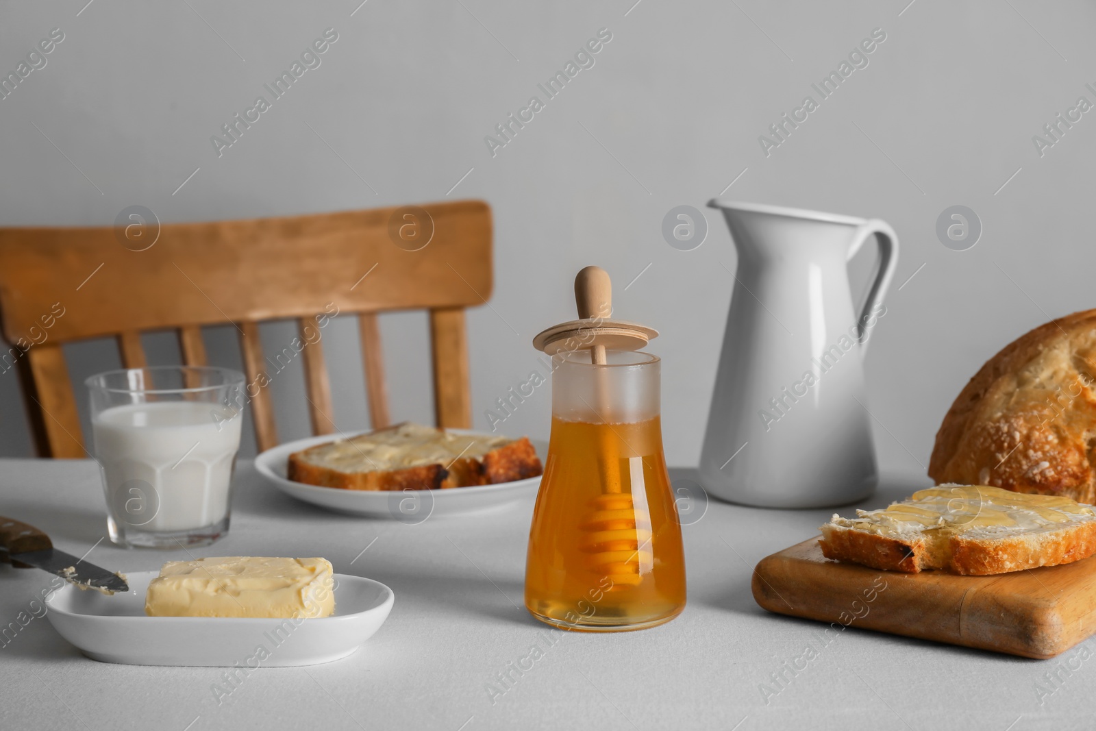 Photo of Delicious honey, milk and bread with butter served for breakfast on table indoors