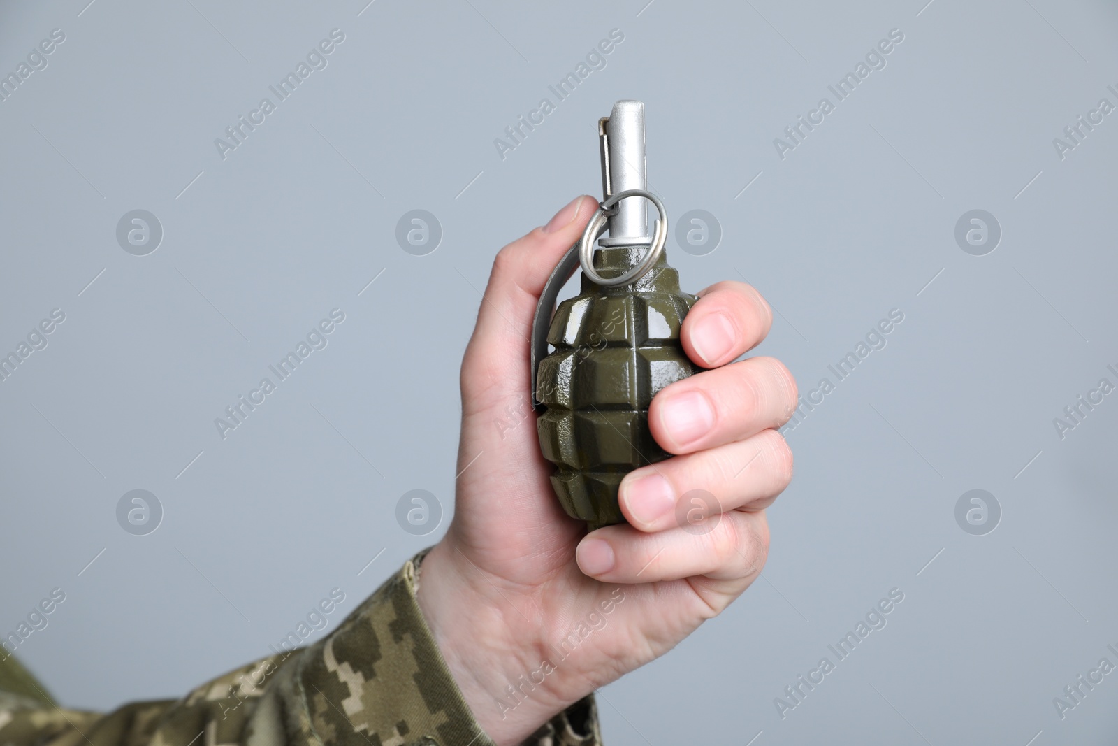 Photo of Soldier holding hand grenade on light grey background, closeup. Military service