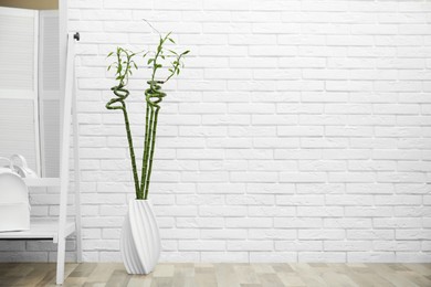 Vase with green bamboo stems and mirror on floor near white brick wall in room, space for text. Interior design