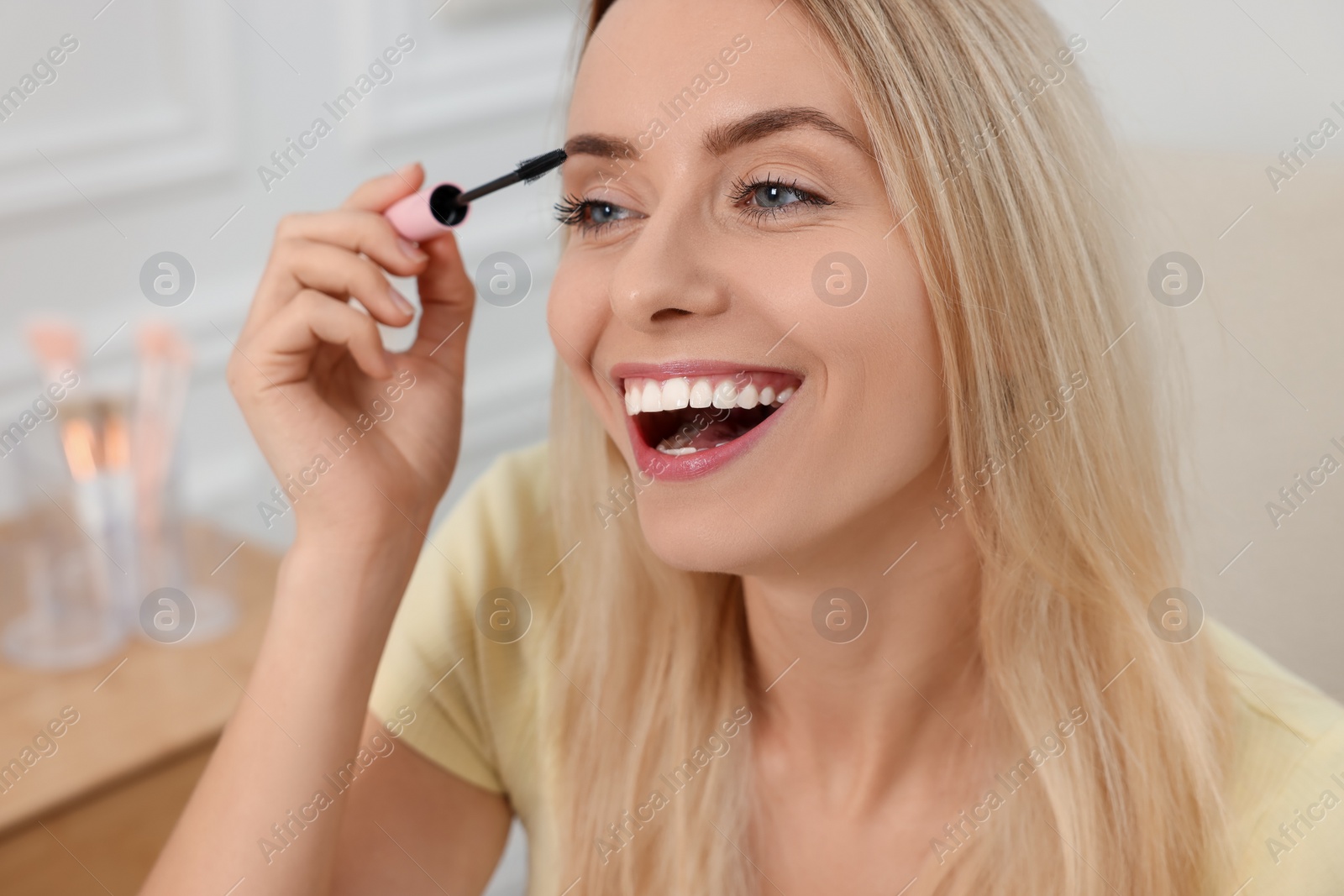 Photo of Beautiful happy woman applying mascara indoors, closeup