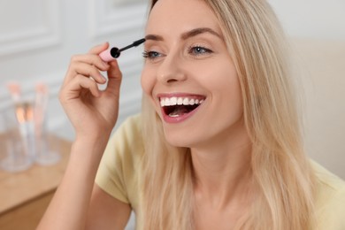 Photo of Beautiful happy woman applying mascara indoors, closeup