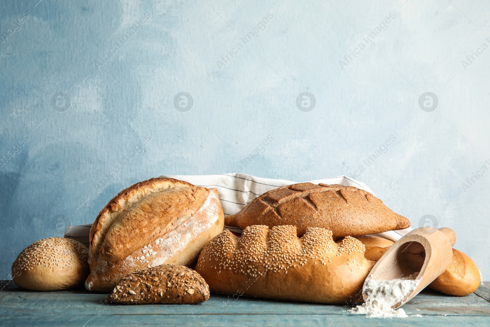 Photo of Fresh bread and scoop of flour on table against color background. Space for text