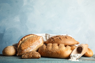 Photo of Fresh bread and scoop of flour on table against color background. Space for text