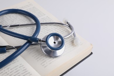 Photo of Open student textbook and stethoscope on white background, closeup. Medical education