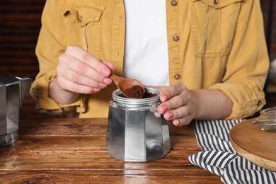 Woman putting ground coffee into moka pot at wooden table, closeup