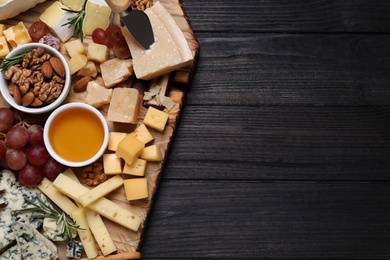 Photo of Cheese plate with honey, grapes and nuts on black wooden table, top view. Space for text