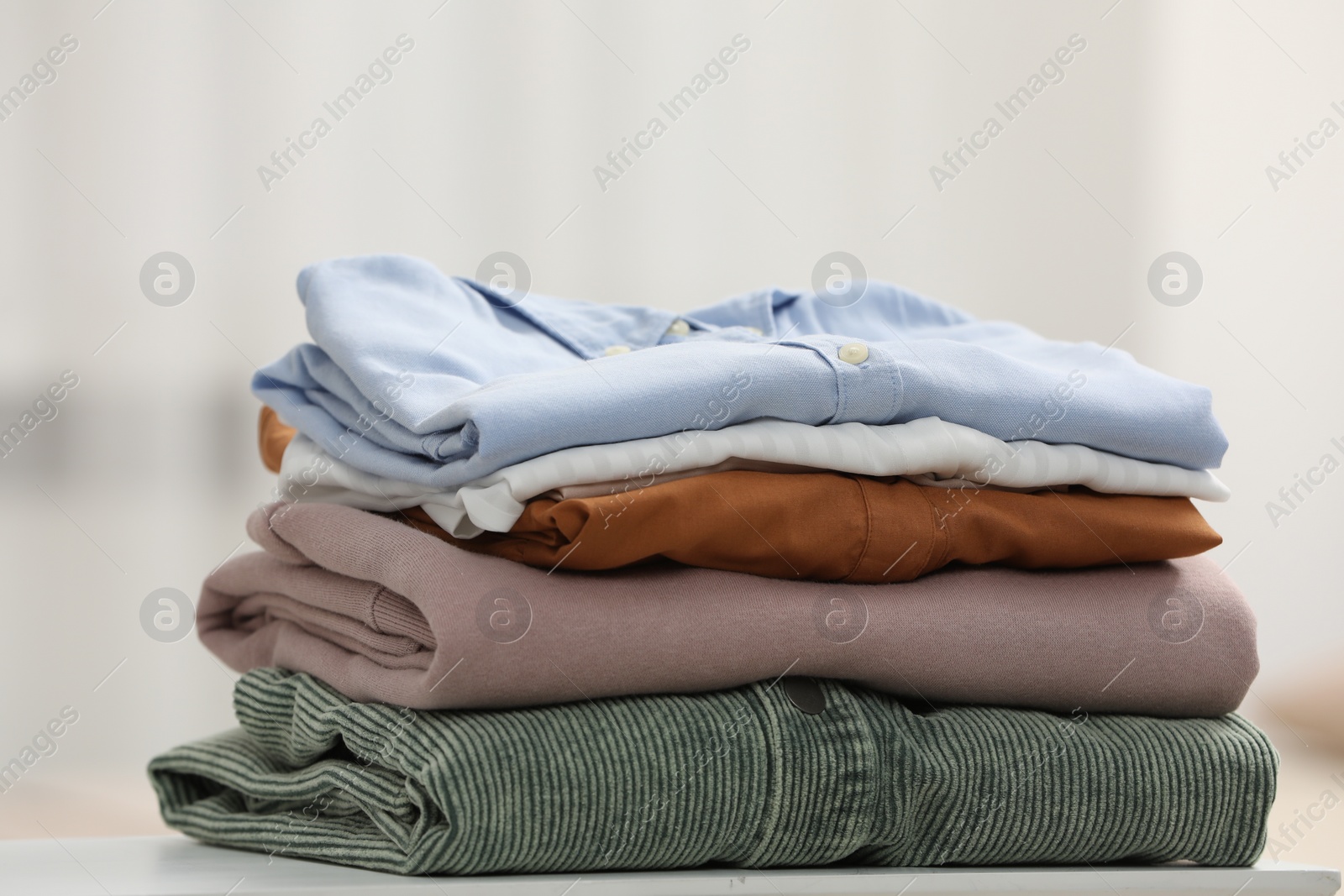 Photo of Stack of different folded clothes white on table, closeup