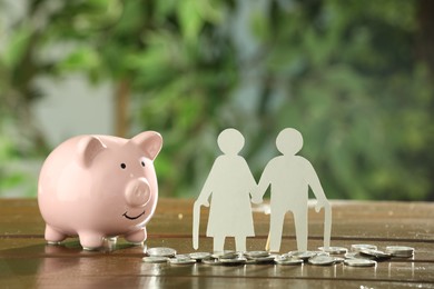 Photo of Pension savings. Figures of senior couple, piggy bank coins on wooden table outdoors