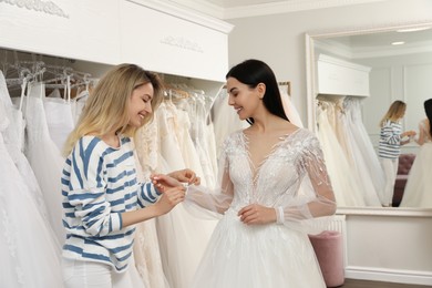 Woman helping bride wear wedding dress in boutique