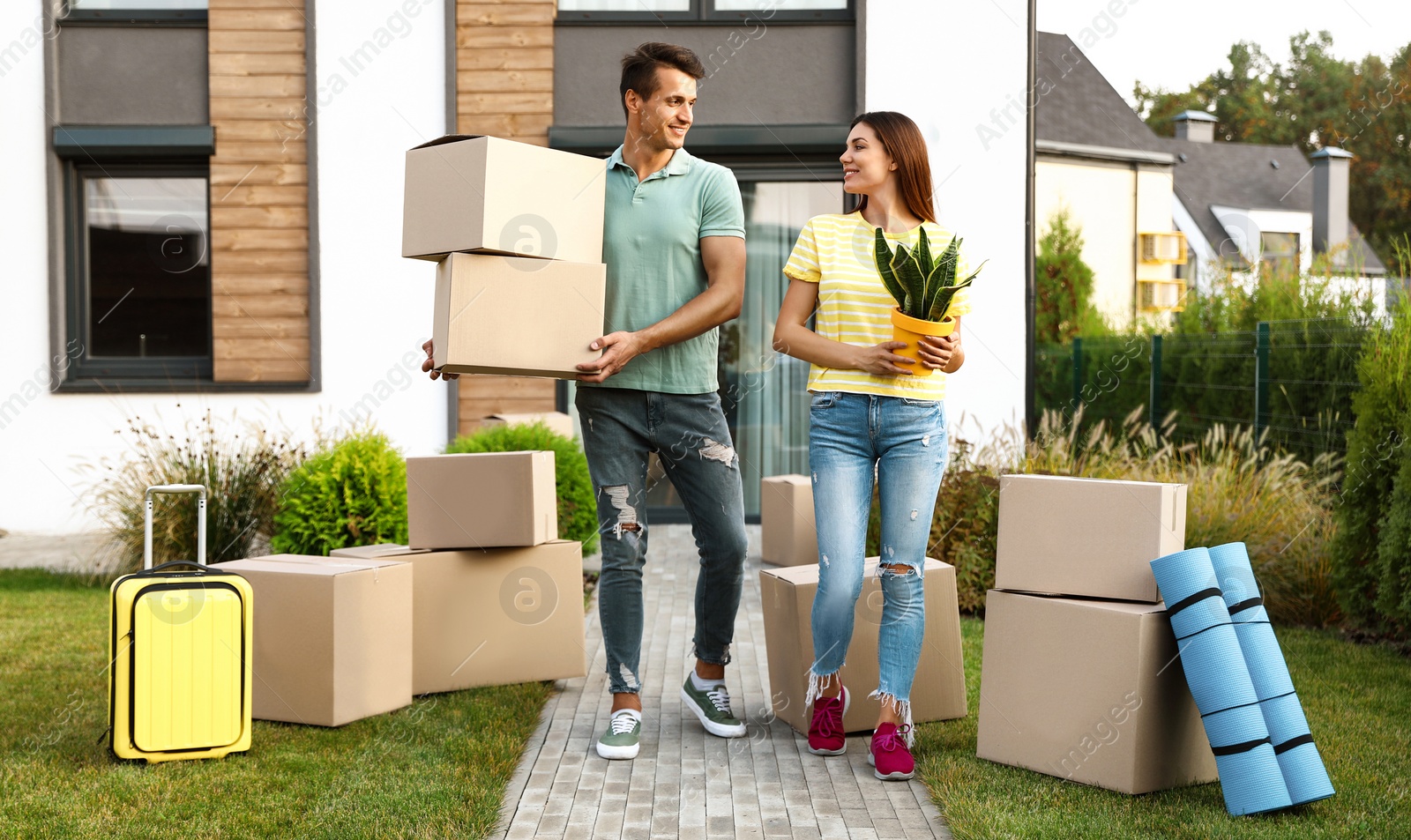 Photo of Happy couple with moving boxes and household stuff near their new house on sunny day