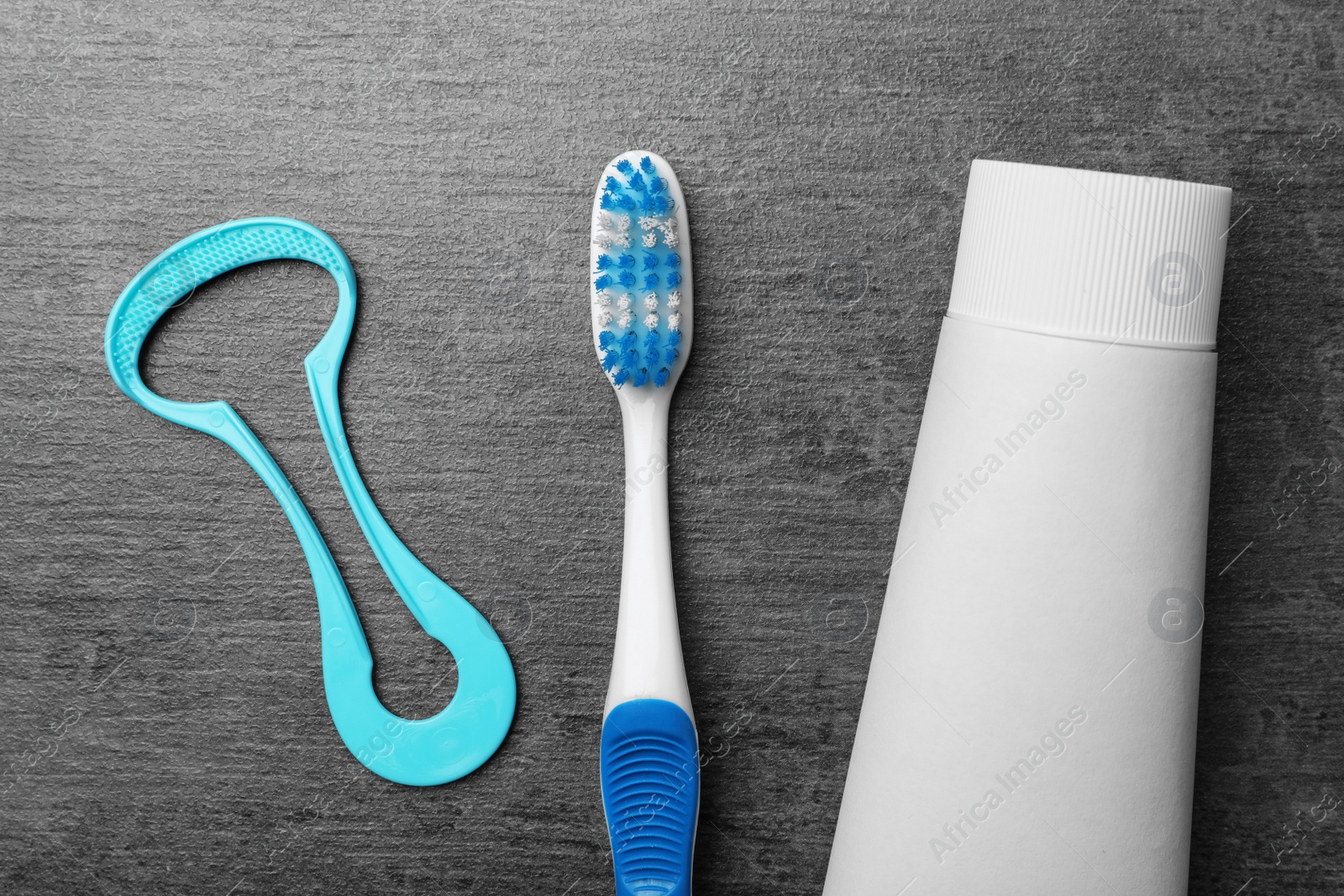 Photo of Tongue cleaner, tooth paste and brush on grey background, flat lay