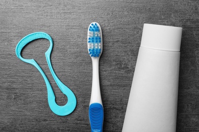 Photo of Tongue cleaner, tooth paste and brush on grey background, flat lay