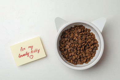 Photo of Feeding bowl of kibble with cat ears and cute note For My Lovely Kitty on white background, flat lay