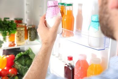 Photo of Man taking bottle with yogurt out of refrigerator in kitchen, closeup