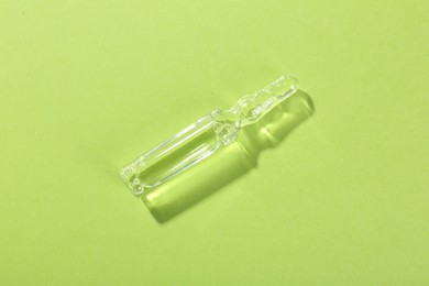 Photo of Glass ampoule with liquid on light green background, top view