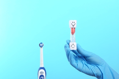 Dentist holding sand glass near electric toothbrush on color background. Space for text