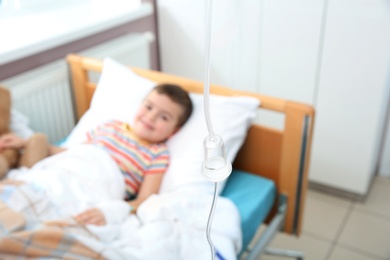 Photo of Little child with intravenous infusion in hospital bed, focus on drip chamber