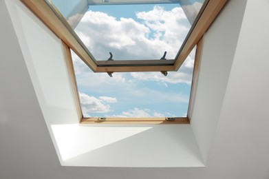 Open skylight roof window on slanted ceiling in attic room, bottom view