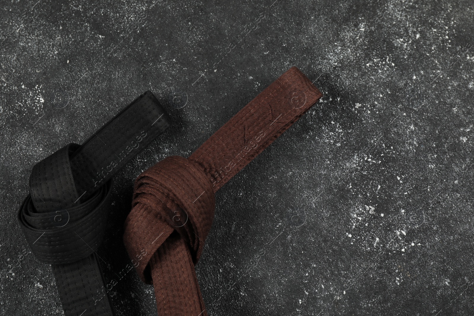 Photo of Black and brown karate belts on gray textured background, flat lay. Space for text