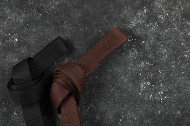 Photo of Black and brown karate belts on gray textured background, flat lay. Space for text