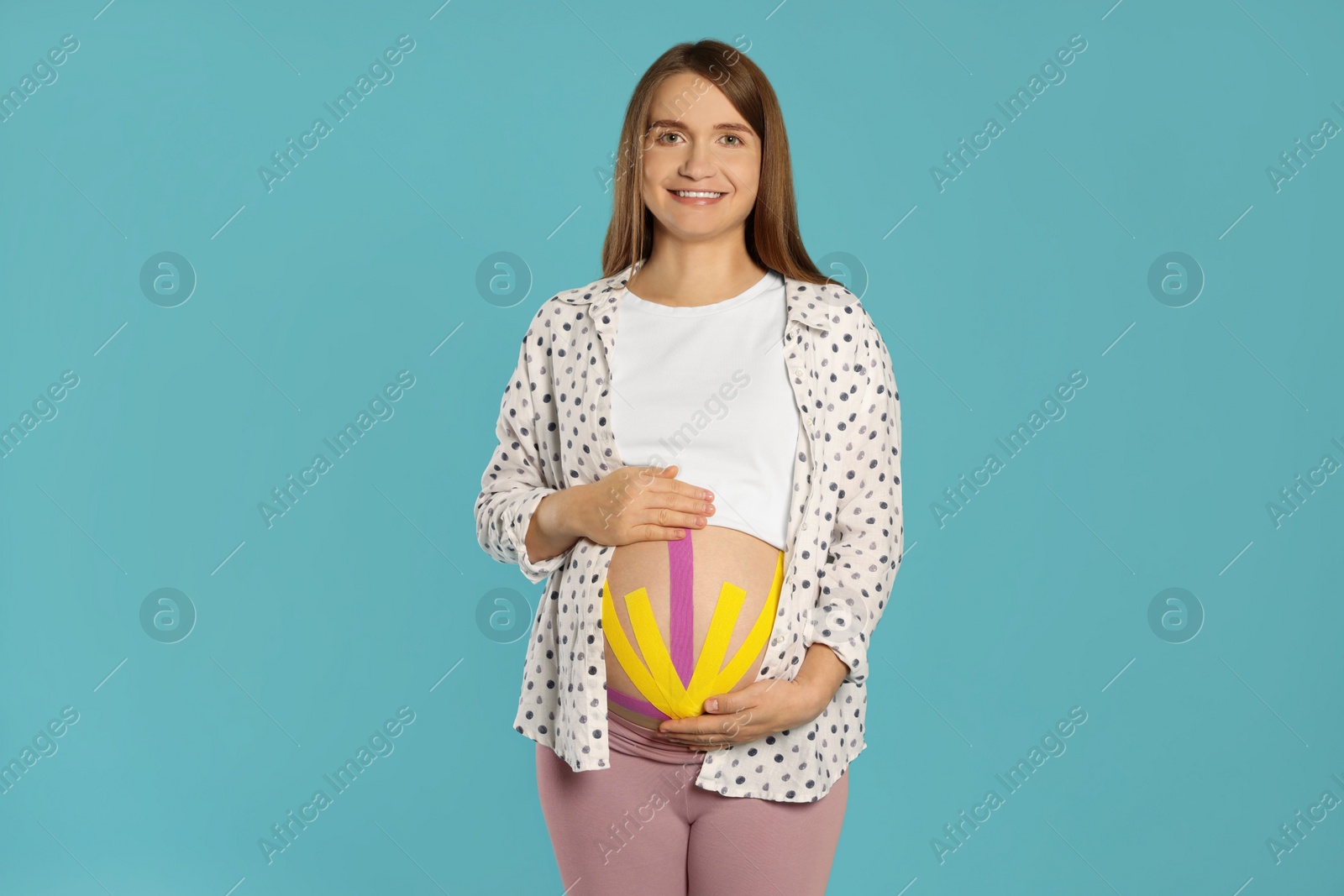 Photo of Pregnant woman with kinesio tapes on her belly against light blue background